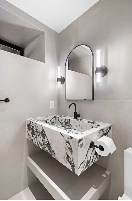 Marble basin with black tap and arched mirror in micro cement