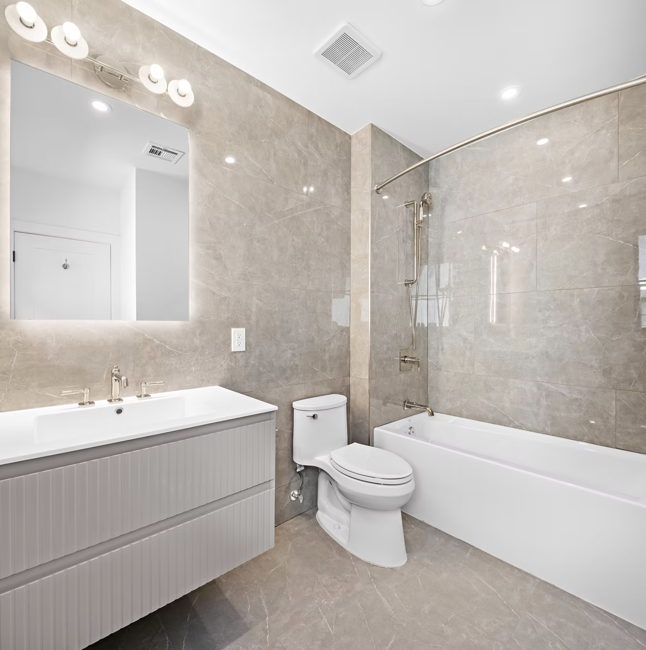 Guest bathroom in stone tile with bath and backlit mirror
