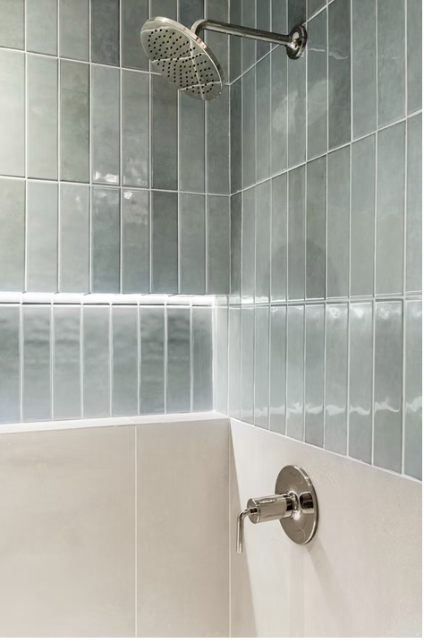 Shower with stacked green tile and lit niche detail
