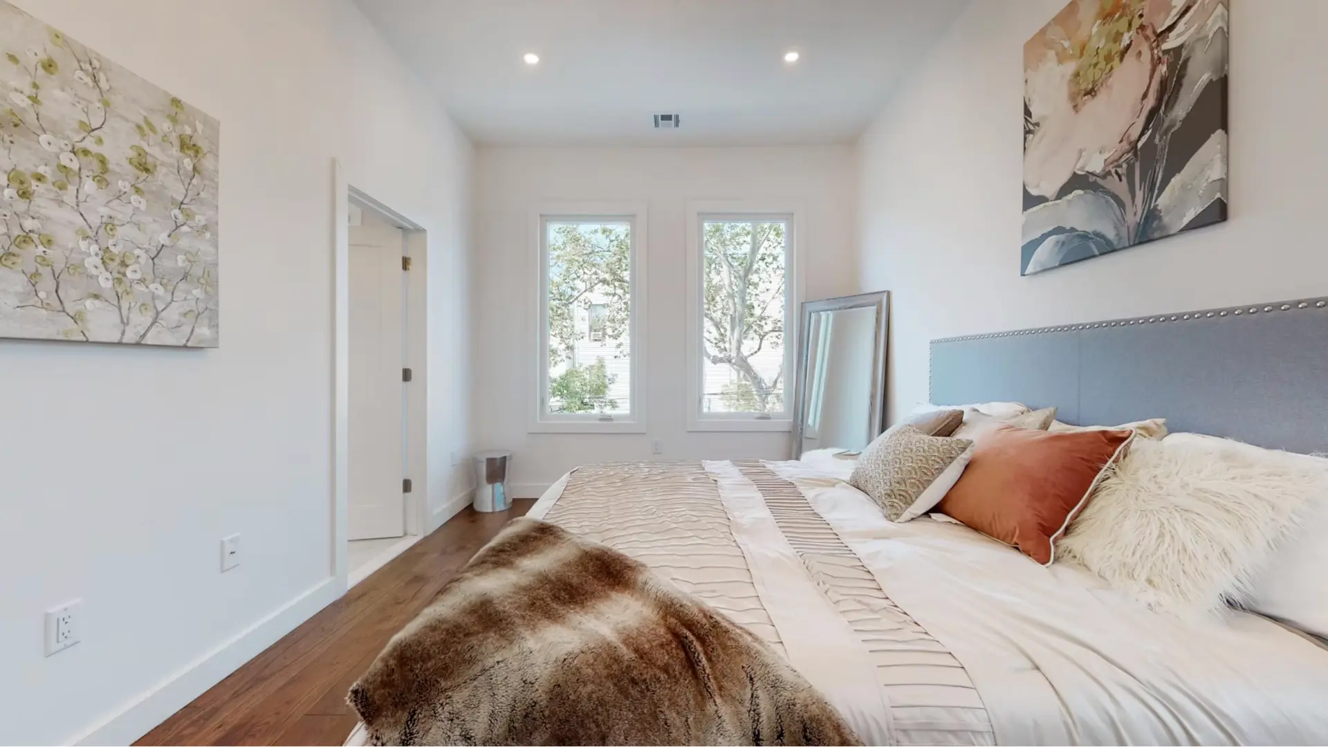 Bright bedroom with hardwood flooring, twin windows and upholstered bed