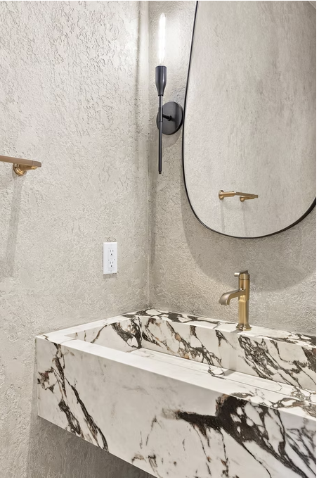 Sculptural marble basin with brass tap and black framed mirror
