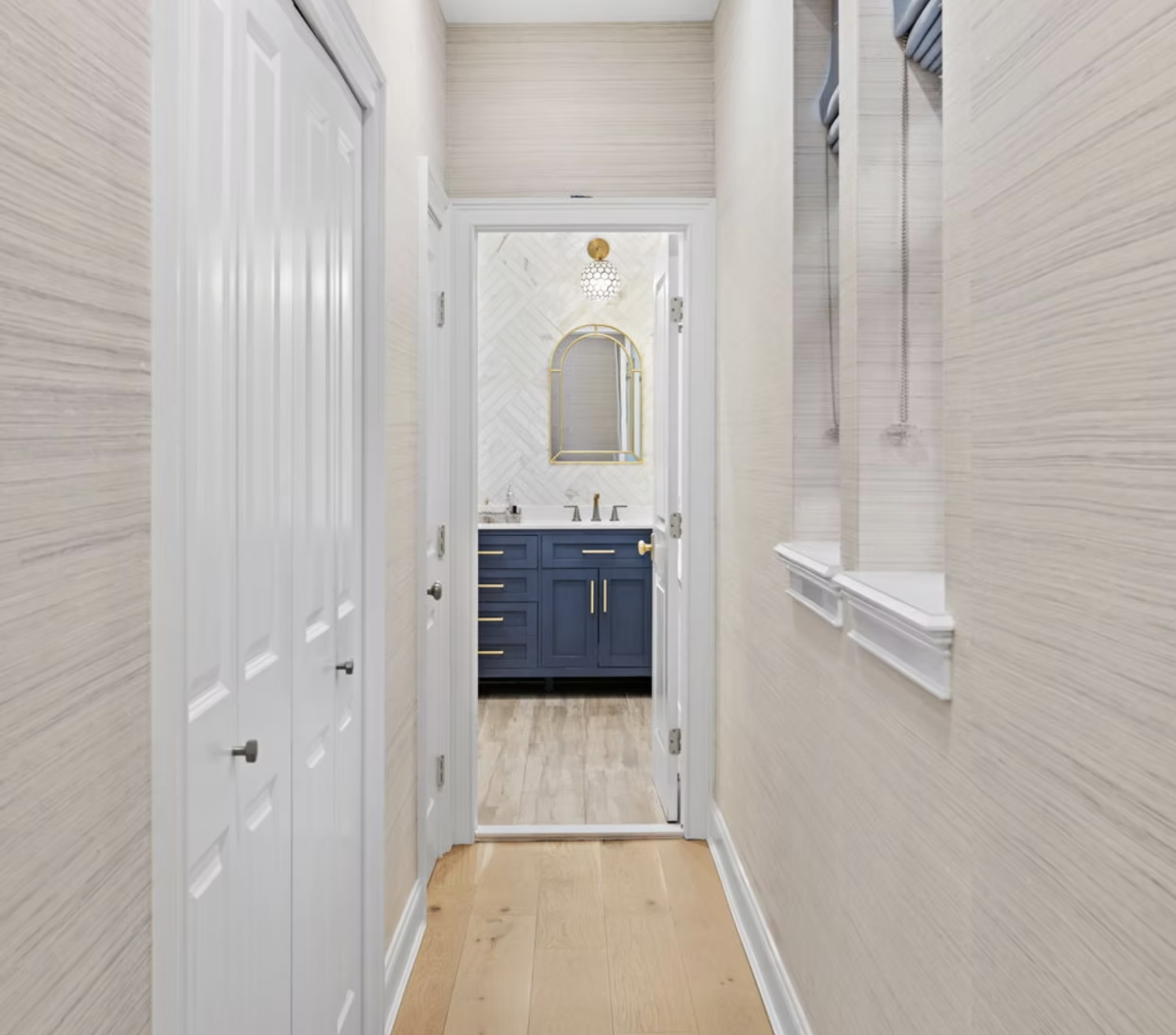 Hallway with grasscloth walls leading to a navy vanity cloakroom