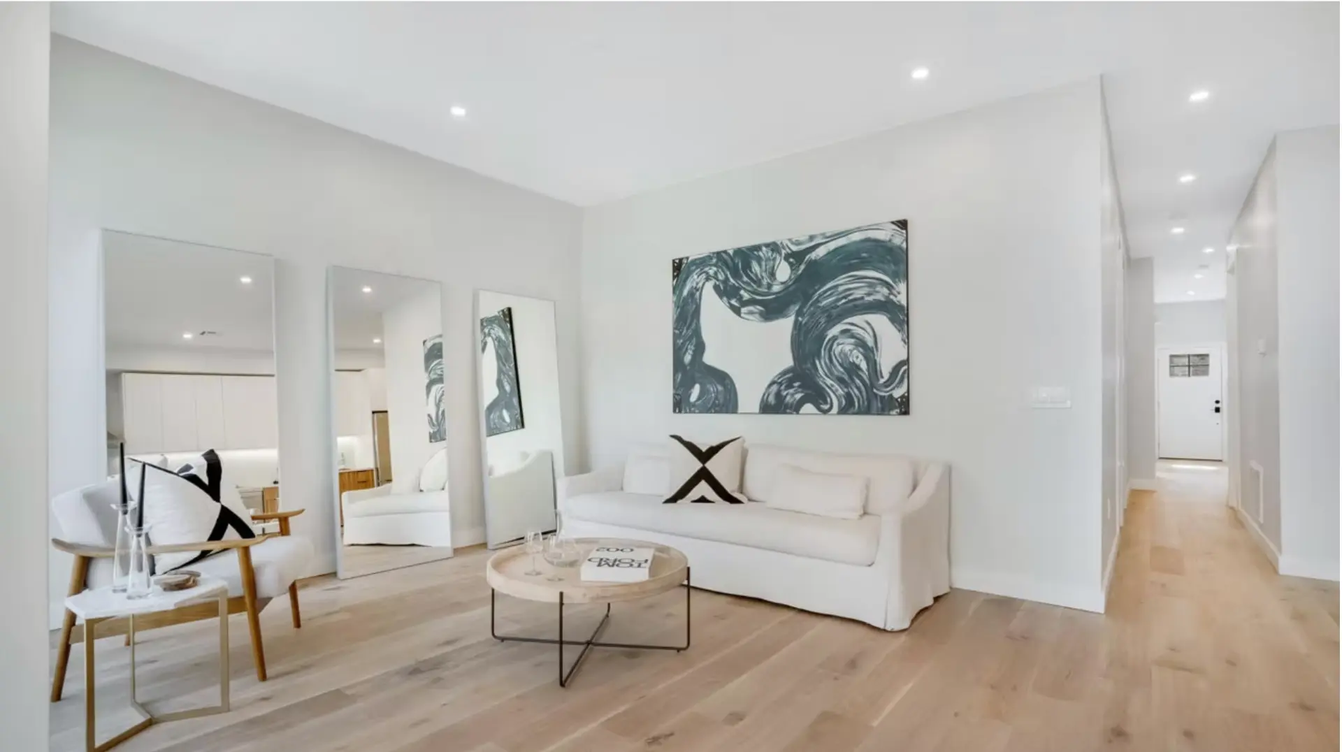 Bright minimal living room with oak flooring and leaning mirrors